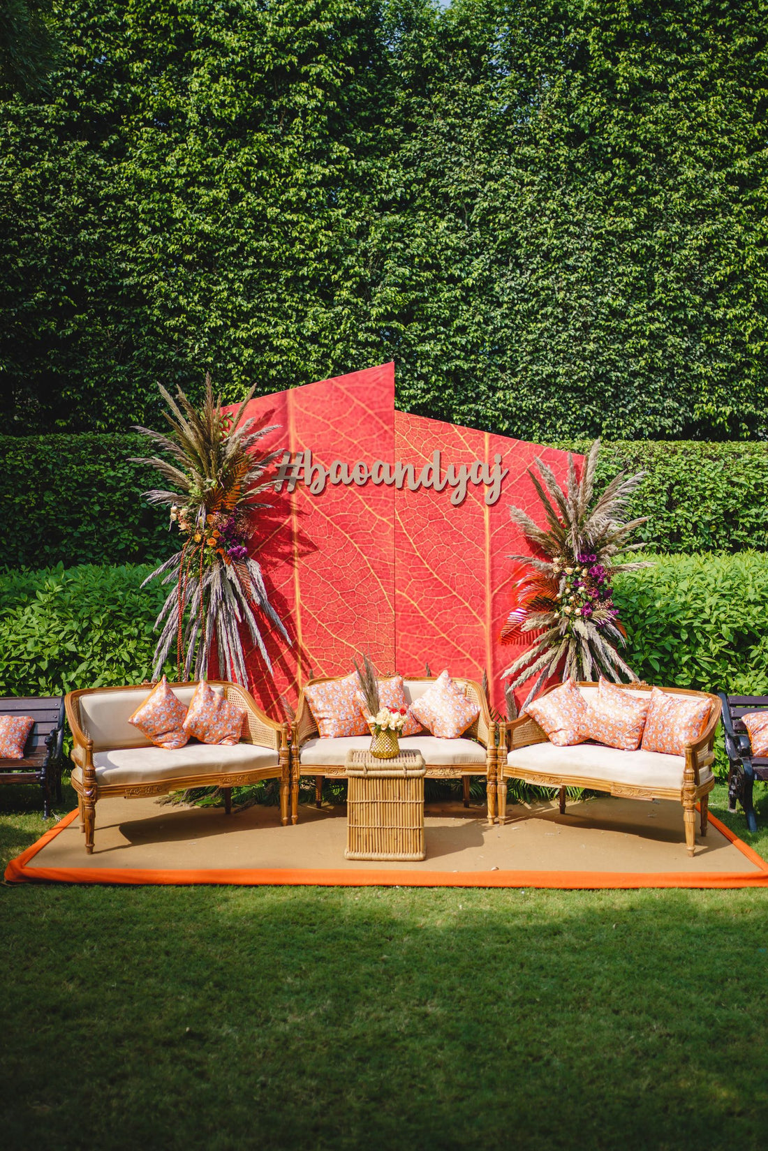 Outdoor wedding lounge with floral backdrop, chairs and colorful cushions