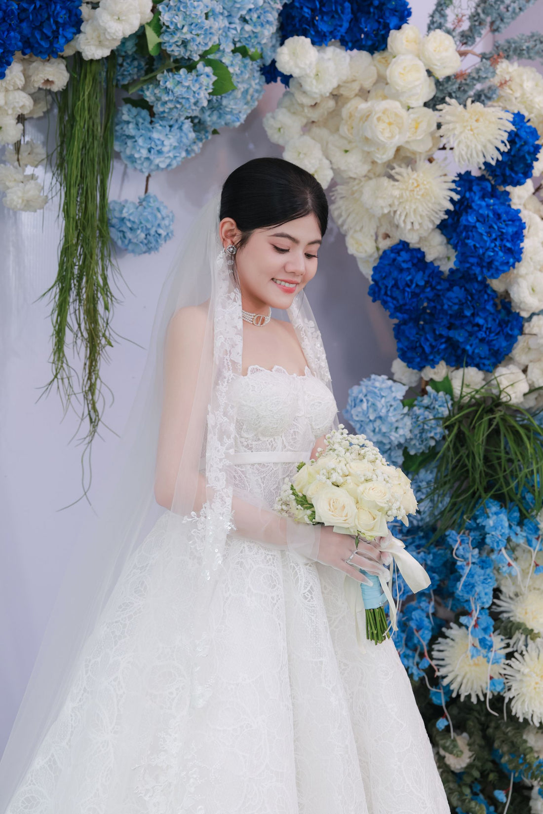 Bride in a white dress holding a bouquet in front of a blue and white floral backdrop