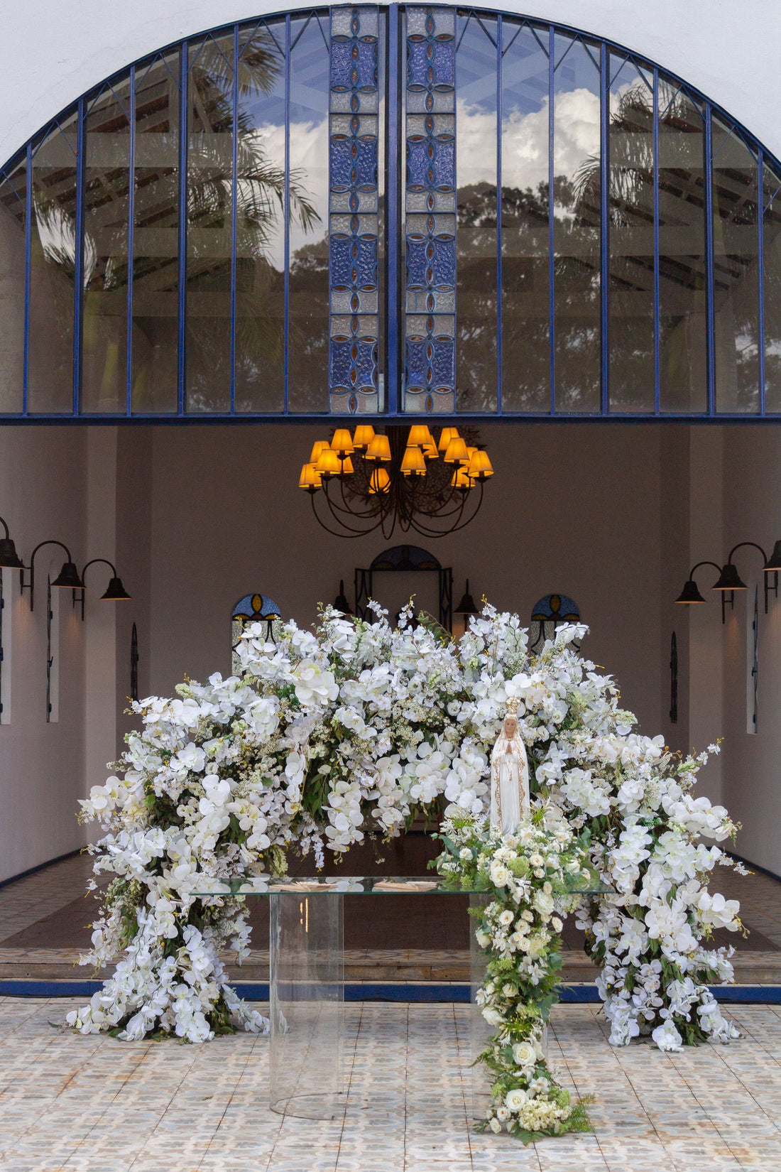 White floral wedding arch inside a chapel with blue accents and stained glass