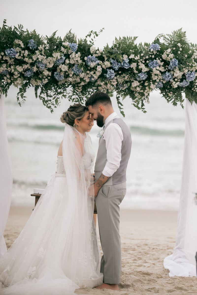 Couple at a beach wedding ceremony beneath a floral arch beside the ocean