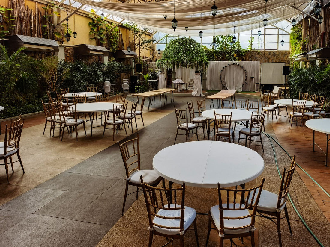 Empty indoor wedding venue with round tables, chairs, and greenery