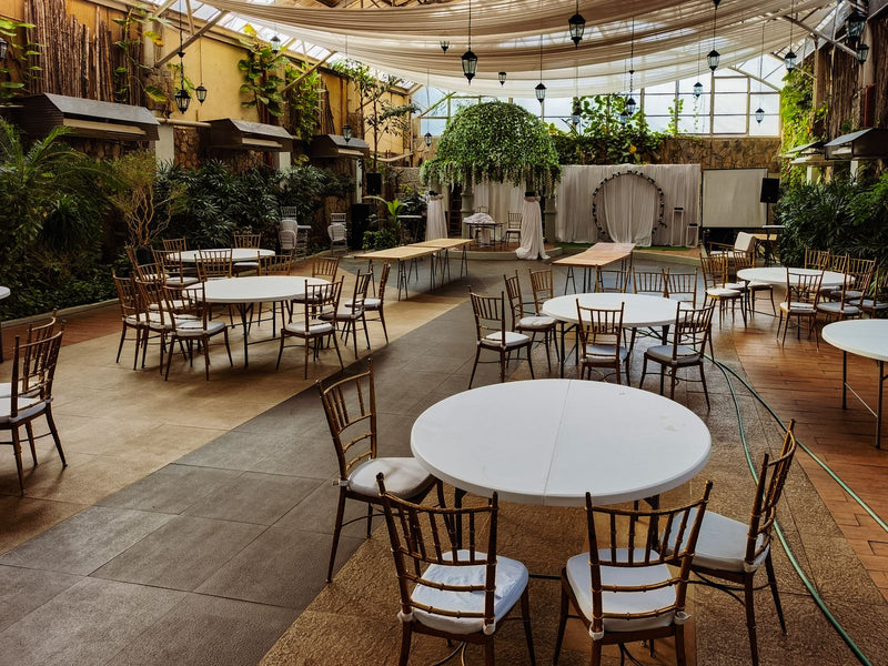 Empty indoor wedding venue with round tables, chairs, and greenery