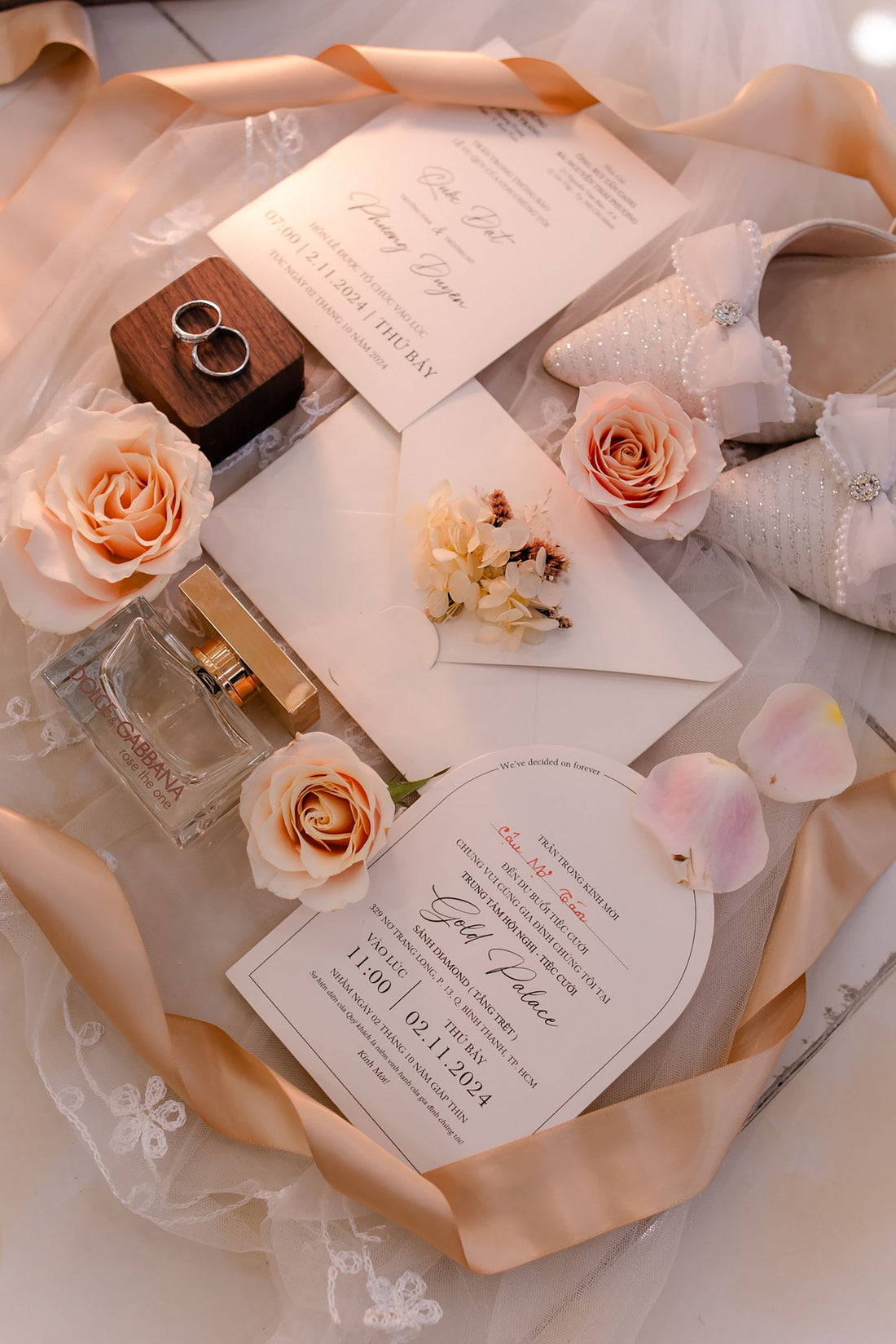 Wedding invitation flat lay with pink flowers, rings, ribbon and shoes