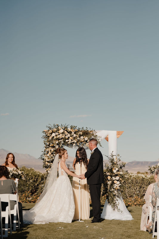 Outdoor wedding ceremony with a couple and guests gathered beneath a floral arch