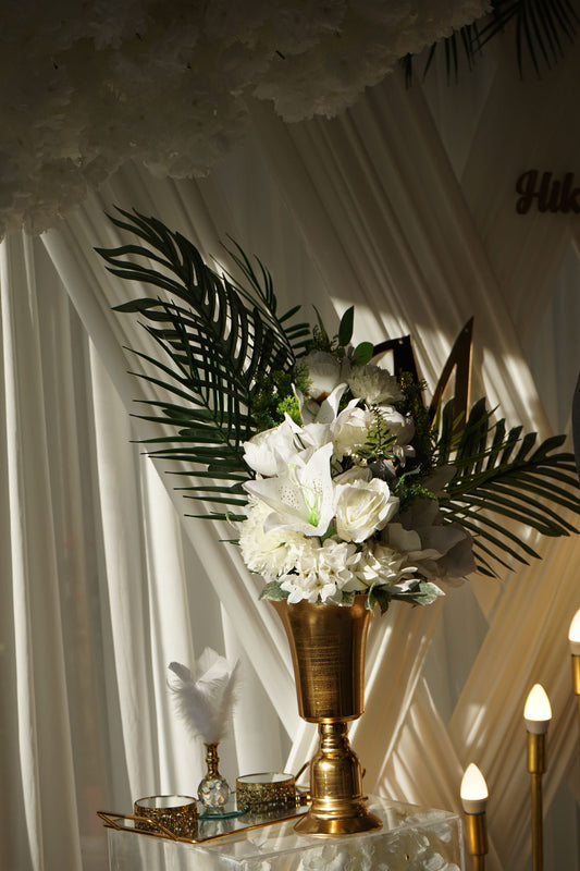 White wedding floral arrangement displayed in a gold vase against softly draped fabric