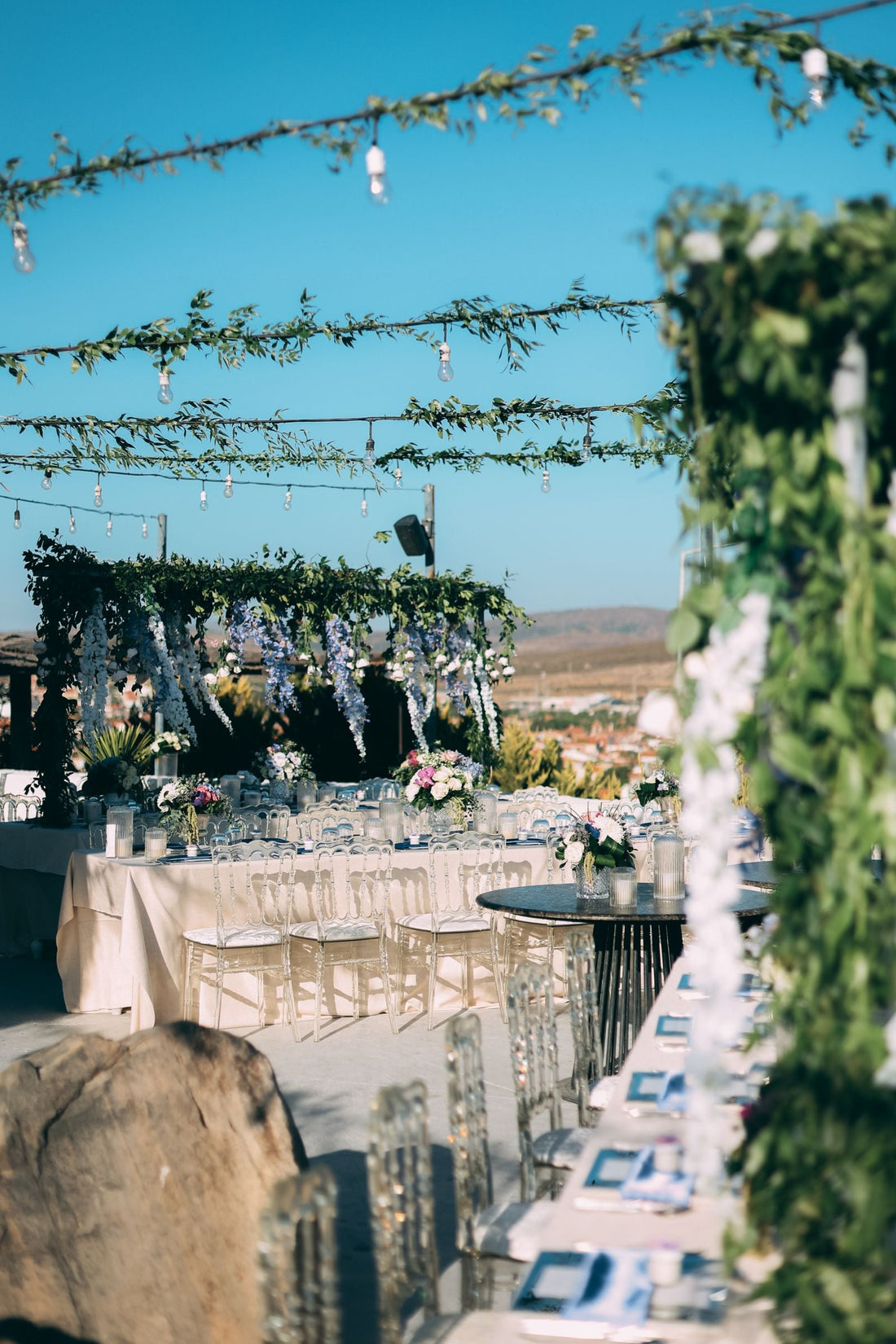 Outdoor wedding reception beneath a green floral canopy with decorated tables and clear chairs