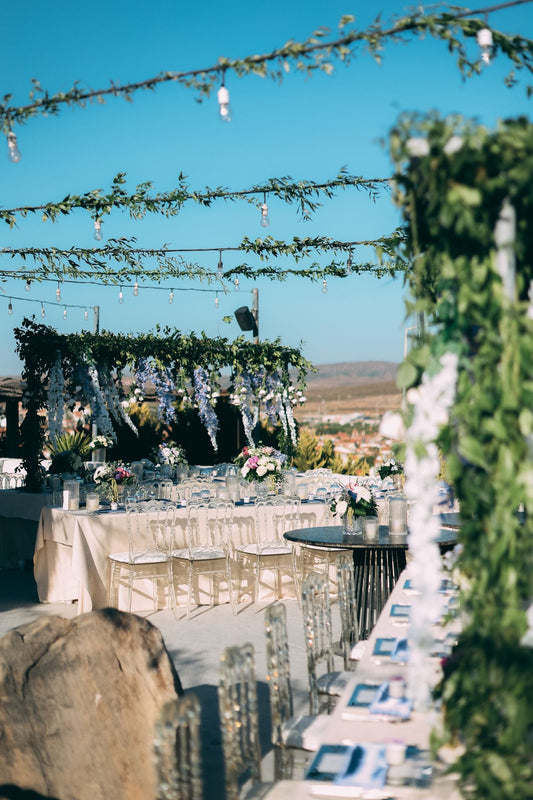 Outdoor wedding reception beneath a green floral canopy with decorated tables and clear chairs