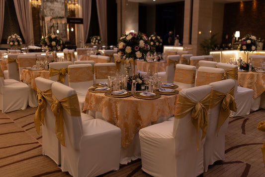 Large indoor wedding reception hall with round tables, floral arrangements, chandeliers, and clear aisles