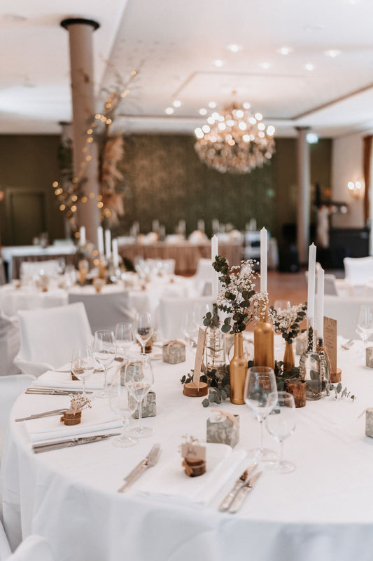 Indoor wedding reception with round tables, floral decorations, candles, and warm chandelier lighting