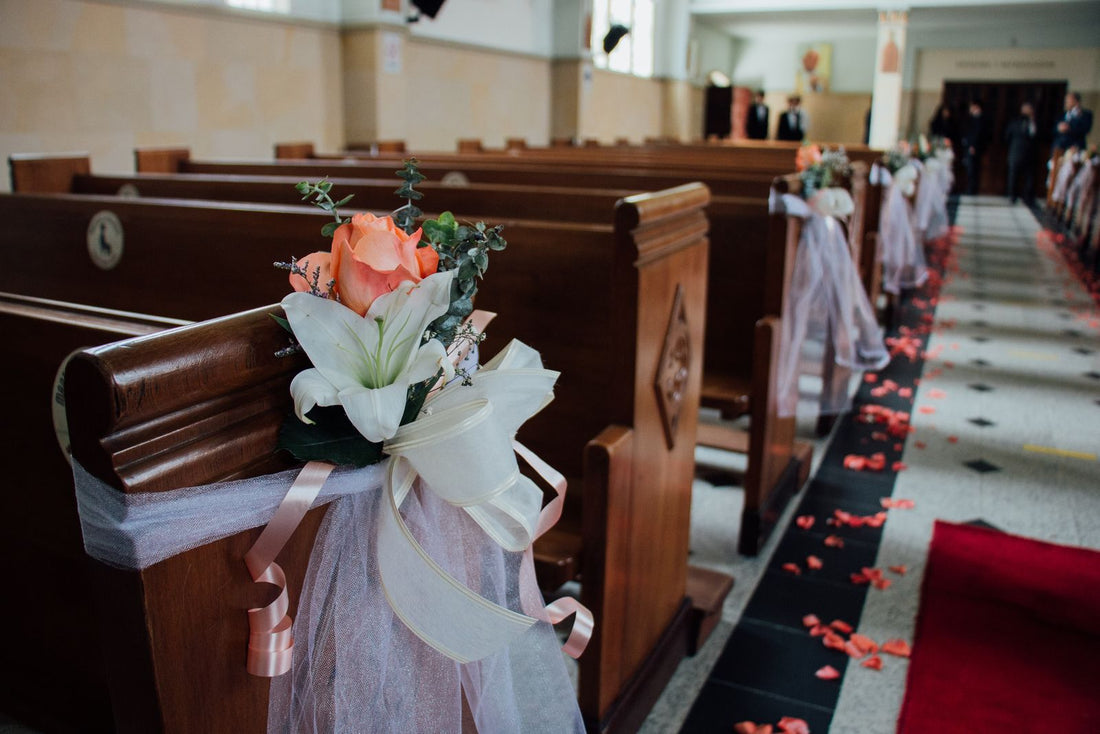 Indoor wedding aisle with rose petals and floral arrangements attached to wooden pews