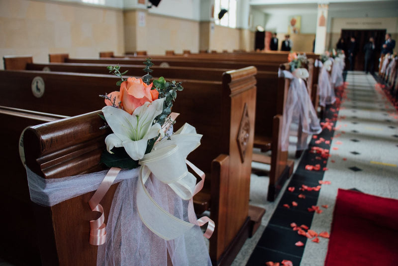 Indoor wedding aisle with rose petals and floral arrangements attached to wooden pews