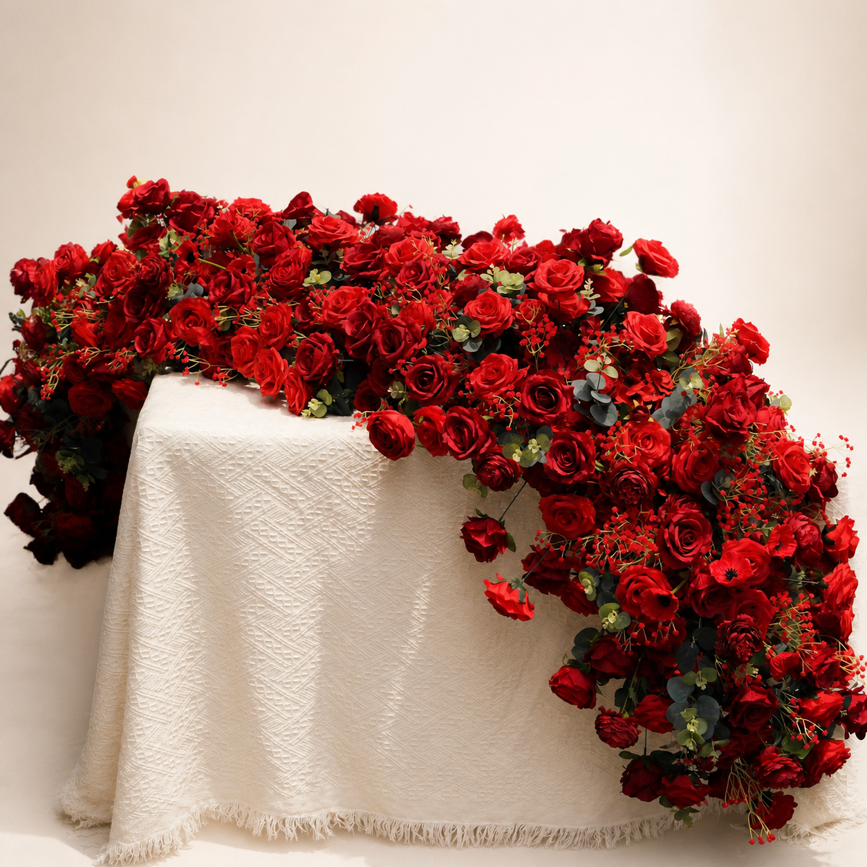 Long red rose artificial flower runner draped over an ivory table in warm white studio
